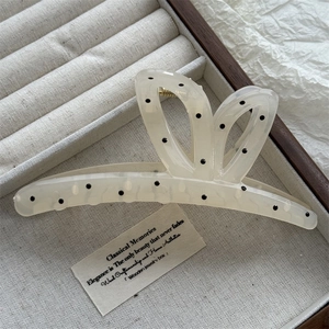 Close-up of a cream hair claw with black polka dots on a grey velvet jewelry tray