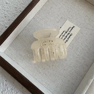 Detail of a creamy beige square hair claw clip with golden text in a wooden tray