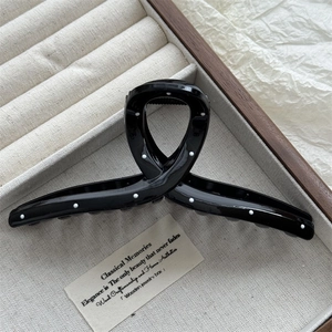 Detailed view of a black high-gloss hair claw clip with white polka dots on a linen tray