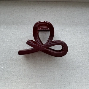Detail view of glossy burgundy hair claw clip featuring a streamlined twist and metal spring