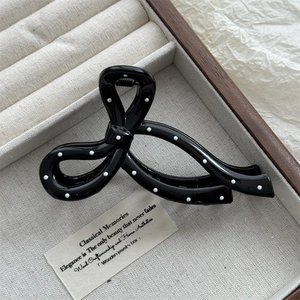 Detailed view of large black bow hair claw clip with white polka dots on jewelry box