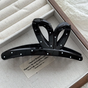 Close-up of a large black hair claw clip with white polka dots on a linen jewelry tray
