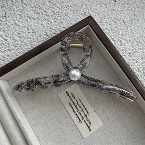 Détail d'une pince à cheveux en résine grise avec maille de dentelle et perle élégante
