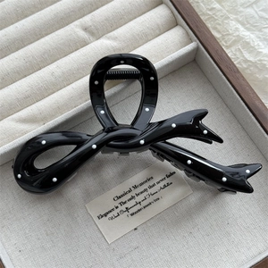 Close-up of a black bow-shaped hair claw clip with white polka dots on a wooden tray