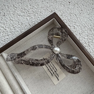 Détail d'une pince à cheveux grise avec motif dentelle noire et perle blanche en coffret