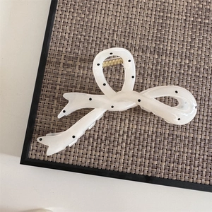 Detail of a creamy white bow hair claw clip with black polka dots and gold metal spring