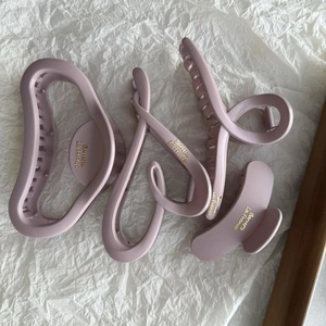Detail of four matte purple hair claws with golden French lettering on white paper