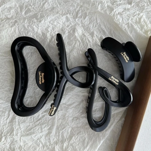 Detail showing four matte black hair claws with elegant gold lettering on white paper