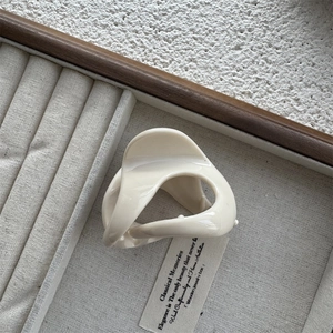 Detail of cream hair claw clip with twisted geometric design on jewelry display tray