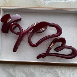 Detail of matte burgundy hair claws with gold text on a wooden tray for women