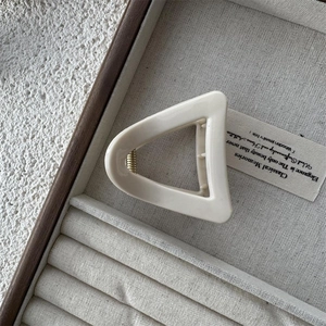 Macro view of cream triangular hair claw clip with golden spring on a wooden tray