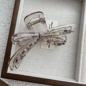Detail view of translucent amber bow hair claw clip with golden text in display box