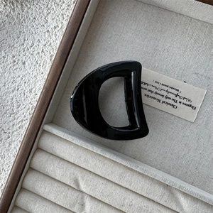 Detail view of large black D-shaped glossy acrylic hair claw clip on a jewelry box display