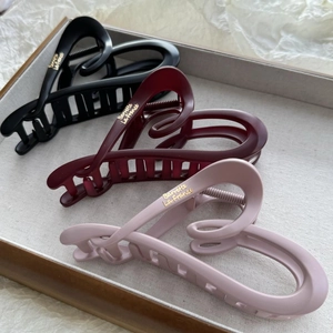 Detail of matte heart-shaped hair claws in black, burgundy, and pink with gold lettering