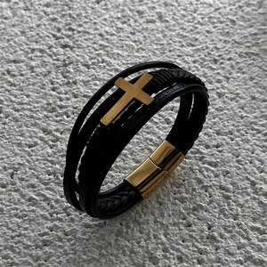 Macro detail of men's multi-layer leather bracelet with gold cross and magnetic clasp