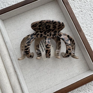 Close-up of leopard print hair claw clip made of glossy acrylic on a wooden tray