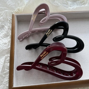 Three matte hair claws in pink, black, and red with gold lettering in a tray