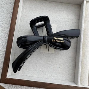 Detail of a black ribbon hair claw clip with golden text in a wooden display tray