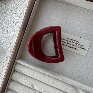 Deep red D-shaped hair claw clip with glossy finish resting in a luxury display box