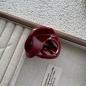 Top view of a glossy burgundy shark hair claw clip on a beige velvet jewelry tray