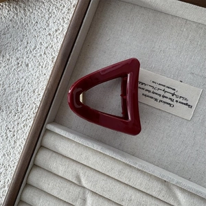 Macro view of a triangular dark red hair claw clip with a glossy finish and metal spring