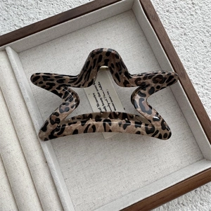 Detailed top view of a star-shaped leopard print hair claw clip on a linen tray