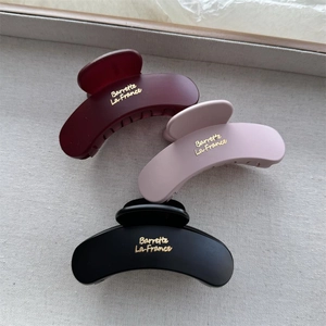 Close-up of matte hair claws in burgundy, pink and black with gold barrette lettering