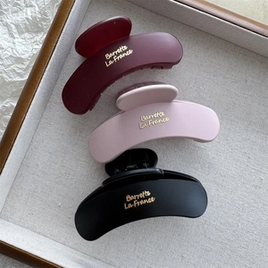 Close-up of three matte hair claws in burgundy, pink and black with gold lettering