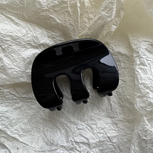 Primo piano della molletta per capelli in resina nera lucida su carta beige testurizzata