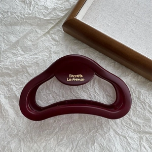 Macro detail of matte burgundy hair claw clip with golden text on textured background