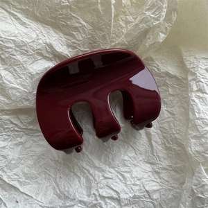 Dettaglio di un fermaglio per capelli bordeaux lucido con design a tre denti su fondo bianco