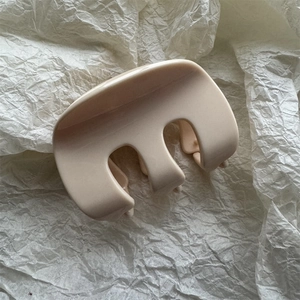 Dettaglio di una pinza per capelli in resina color crema su carta bianca goffrata