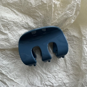 Primo piano di una pinza per capelli blu scuro lucido su sfondo di carta crema strutturata