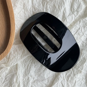 Detail of glossy black geometric hair claw clip on minimalist paper background