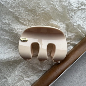 Détail d'une pince à cheveux crème avec un emblème doré Hand Made sur une surface brillante