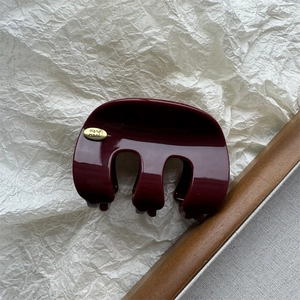 Détail macro de la pince à cheveux bordeaux avec emblème doré Hand made sur papier