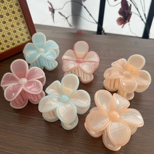 Gros plan de six pinces à cheveux fleur mat en tons macaron sur une surface boisée