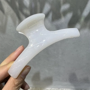 Detail of a white marble pattern hair claw clip held against a shadowed wall