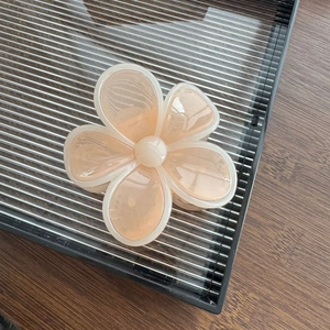 Détail d'une pince à cheveux fleur rose bonbon avec bords blancs et perle centrale
