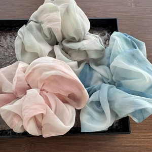 Dettaglio di tre elastici per capelli in chiffon rosa, blu e grigio con motivo sfumato