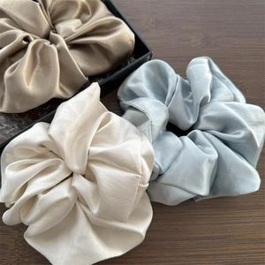 Drei große Satin-Haargummis in Champagner, Beige und Blau auf dunklem Holzhintergrund
