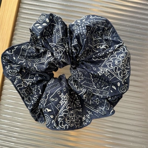 Close-up of navy blue paisley print fabric scrunchie on textured ribbed glass surface