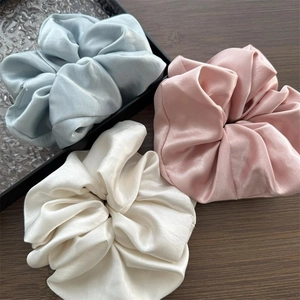 Detailansicht von Seidensatin-Scrunchies in Blau, Rosa und Elfenbein auf Holztablett