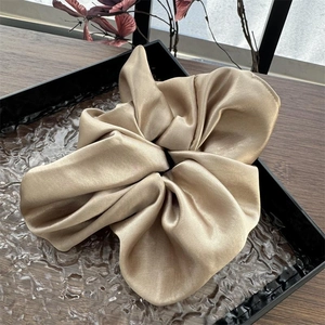 Detailansicht der glänzenden champagner-goldenen Satin-Stofffalten des großen Haargummis