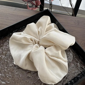 Detaillierte Nahaufnahme von creme satiniertem Oversize-Scrunchie auf hochwertigem Tablett