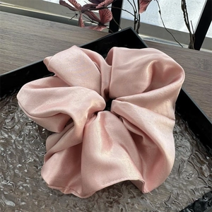Nahaufnahme eines rosa Satin-Haargummis mit Perlglanz-Textur auf einem schwarzen Tablett