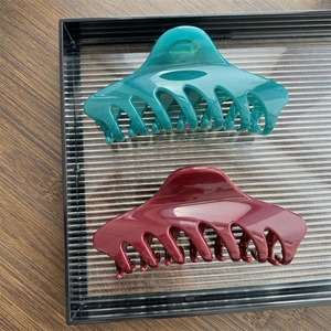 Detailed view of high-gloss hair claws in peacock green and burgundy on a display tray