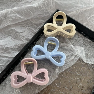 Tre pinze per capelli a fiocco color caramello in beige, blu e rosa su sfondo strutturato