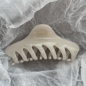 Top view of a large cream acetate hair claw clip on white textured paper background