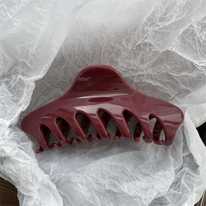 Macro view of deep red glossy hair claw clip showing polished teeth and high shine texture